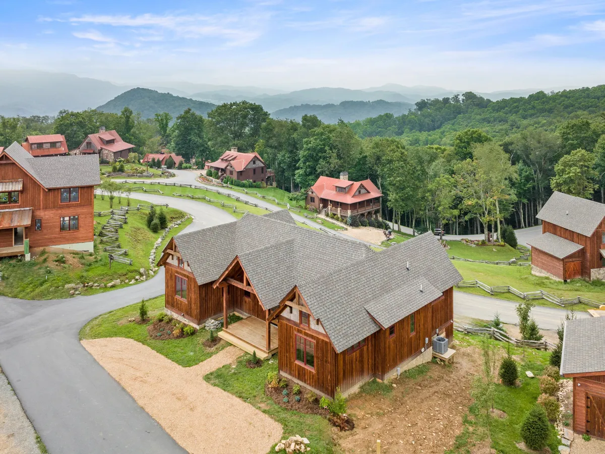 The hero image showcases a brand new wooden cabin set against a stunning mountain backdrop, with a winding road leading through peaceful natural surroundings. The expansive deck invites guests to relax and take in spectacular sunset views, while the setting hints at outdoor adventure and family togetherness.