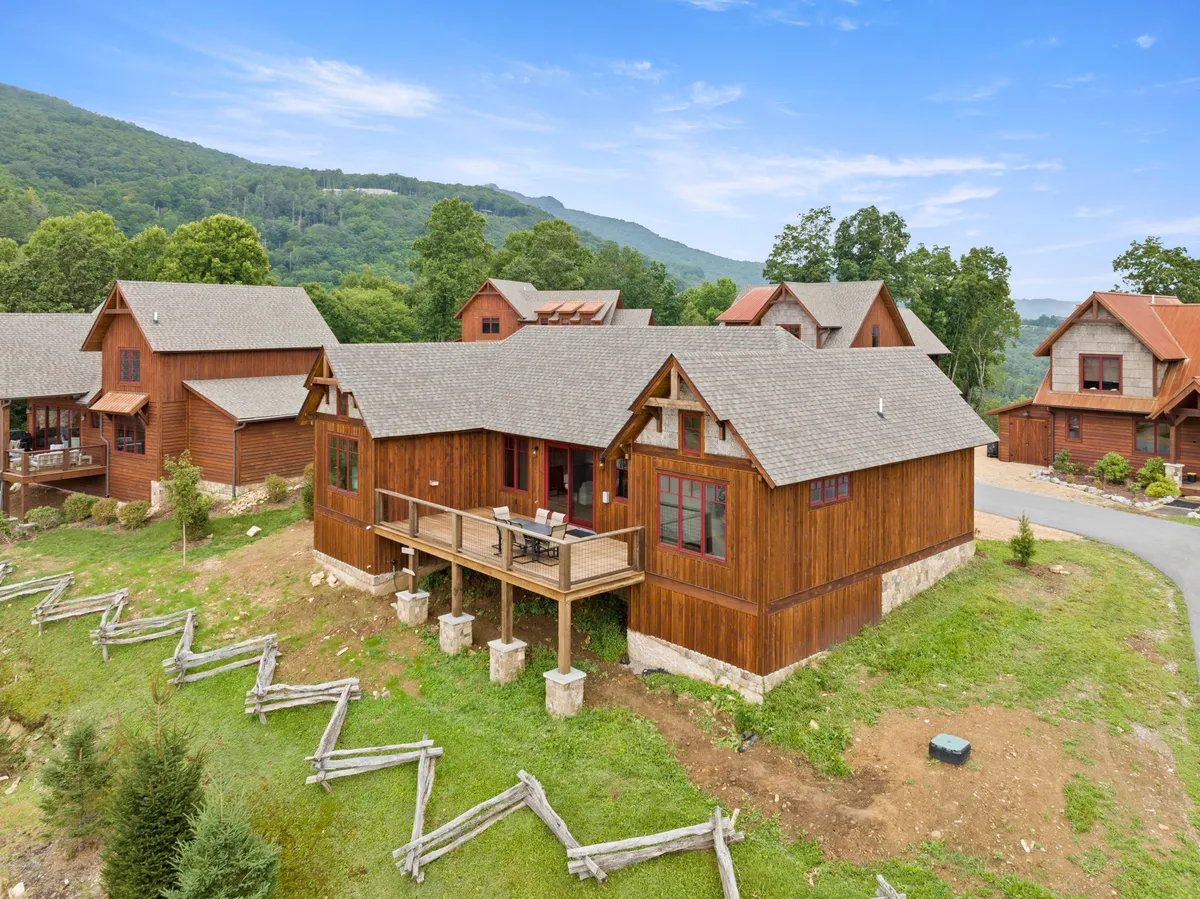 A spacious wooden deck set amidst tall trees, offering sweeping mountain views in the background. The scene is set during sunset, with inviting seating arranged for gatherings or quiet moments. The natural setting and open sky create a welcoming, serene mood ideal for both morning coffees and evening stargazing.
