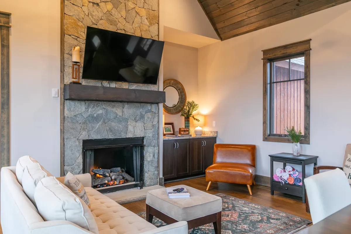 A spacious living area with a stone fireplace, comfortable sofa, wooden accent chair, and a decorative rug, creating a welcoming environment. The scene is perfect for relaxing on cold winter nights and gathering with loved ones after outdoor excursions.