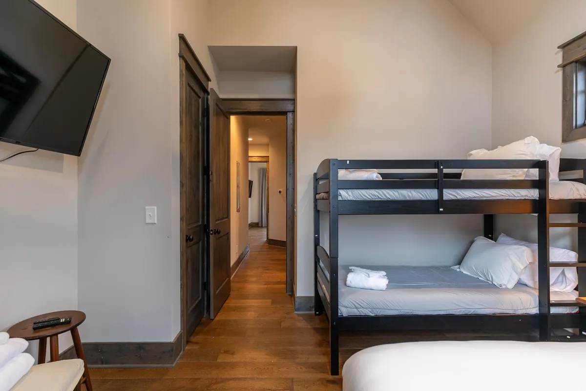 A cozy bedroom featuring bunk beds and a television, with a wooden chair adding character. The space is designed for comfort and fun, ideal for children or teens to unwind after a day of adventure.