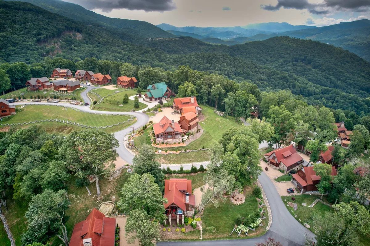A sweeping view of the lush green resort landscape dotted with wooden cabins, winding roads, and a majestic mountain backdrop. The scene reflects the broader community setting and the adventure-filled activities available in the High Country resort environment.