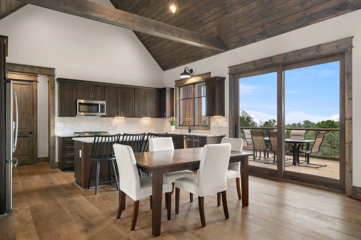 A modern dining area adjacent to a fully equipped kitchen, complete with a kitchen island, sleek appliances, a spacious dining table, and large windows that bathe the space in light and frame scenic views.