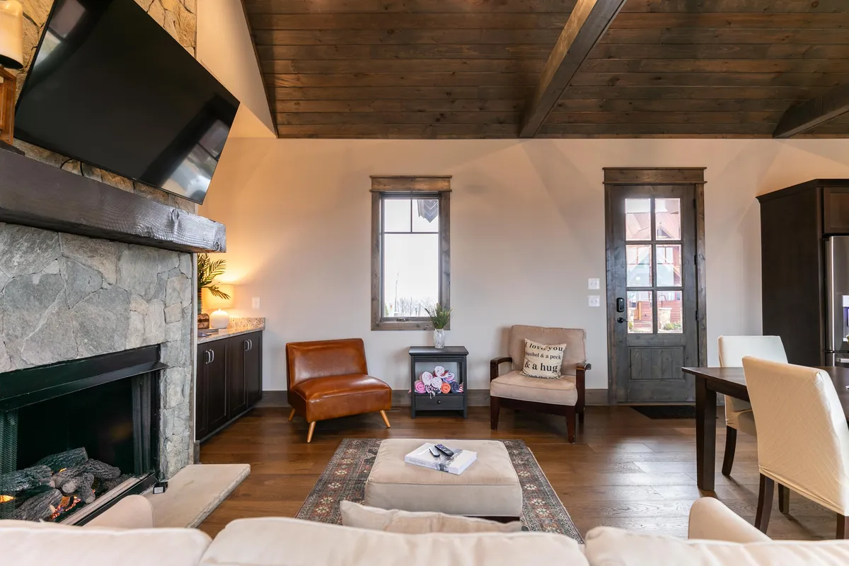 A welcoming living area with a stone fireplace, comfortable sofa, TV, and exposed wooden beams. The room invites socializing, game nights, and relaxing moments together after a day of active exploration.